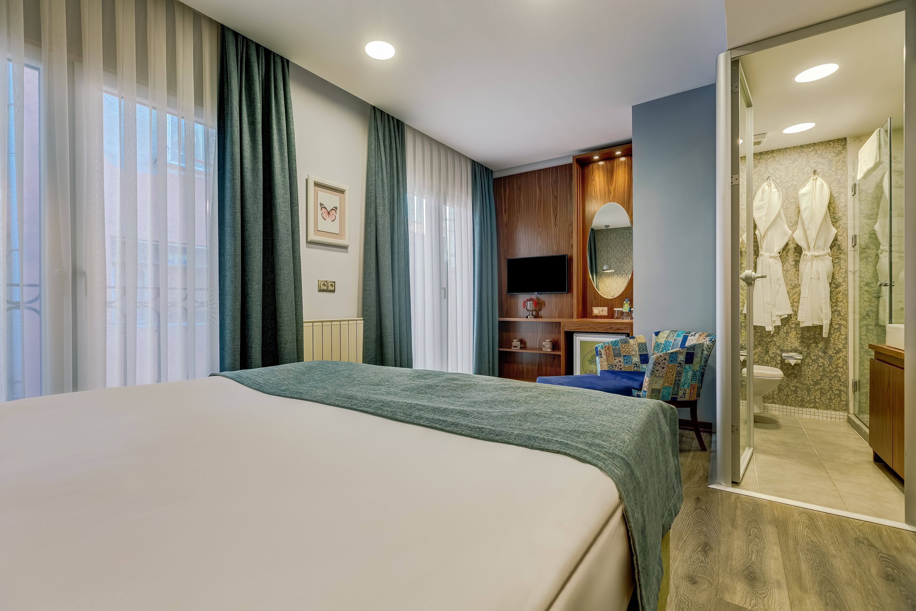 A hotel room with a bed, a TV, a desk with a chair, and a bathroom with a shower and a mirror.