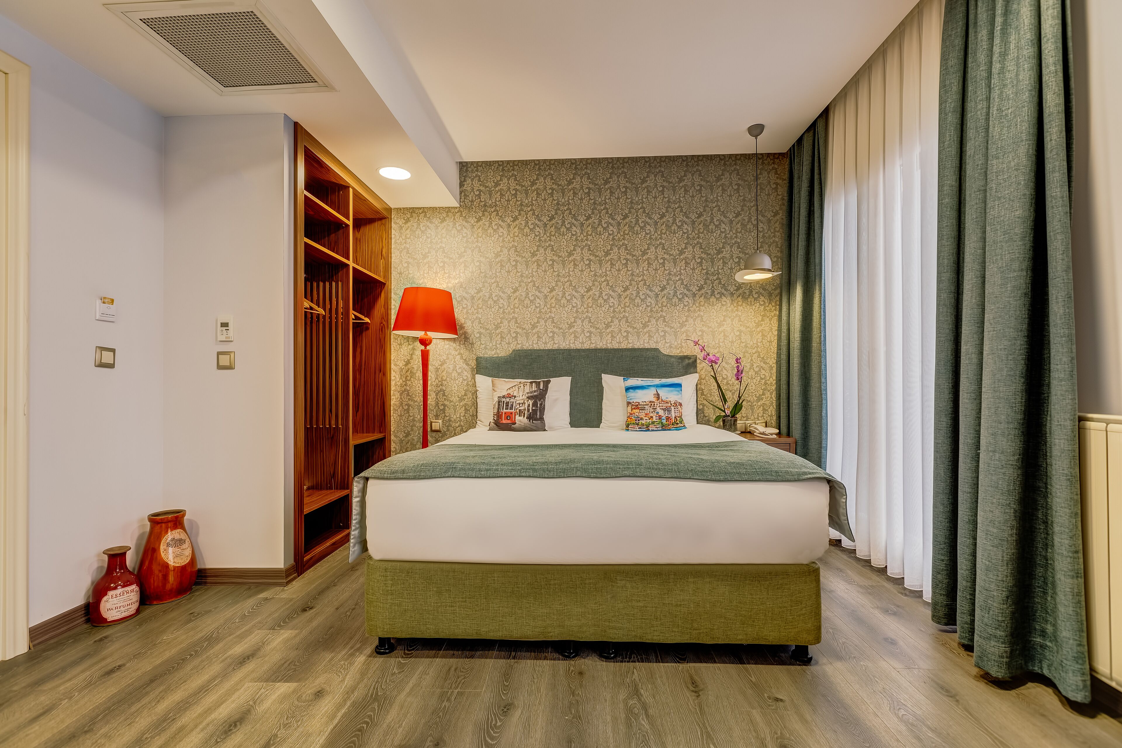 Quarto bem arrumado com cama, guarda-roupa, abajur e um vaso no chão.