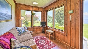 A cozy room with a wooden interior, large windows, a television, a cushioned sofa, and a patterned rug. - Family Getaway w/ Pier on Currituck Sound (Currituck)