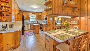 A wooden kitchen with a central island, built-in shelves, and a dining area with a table set for four. - Family Getaway w/ Pier on Currituck Sound (Currituck)