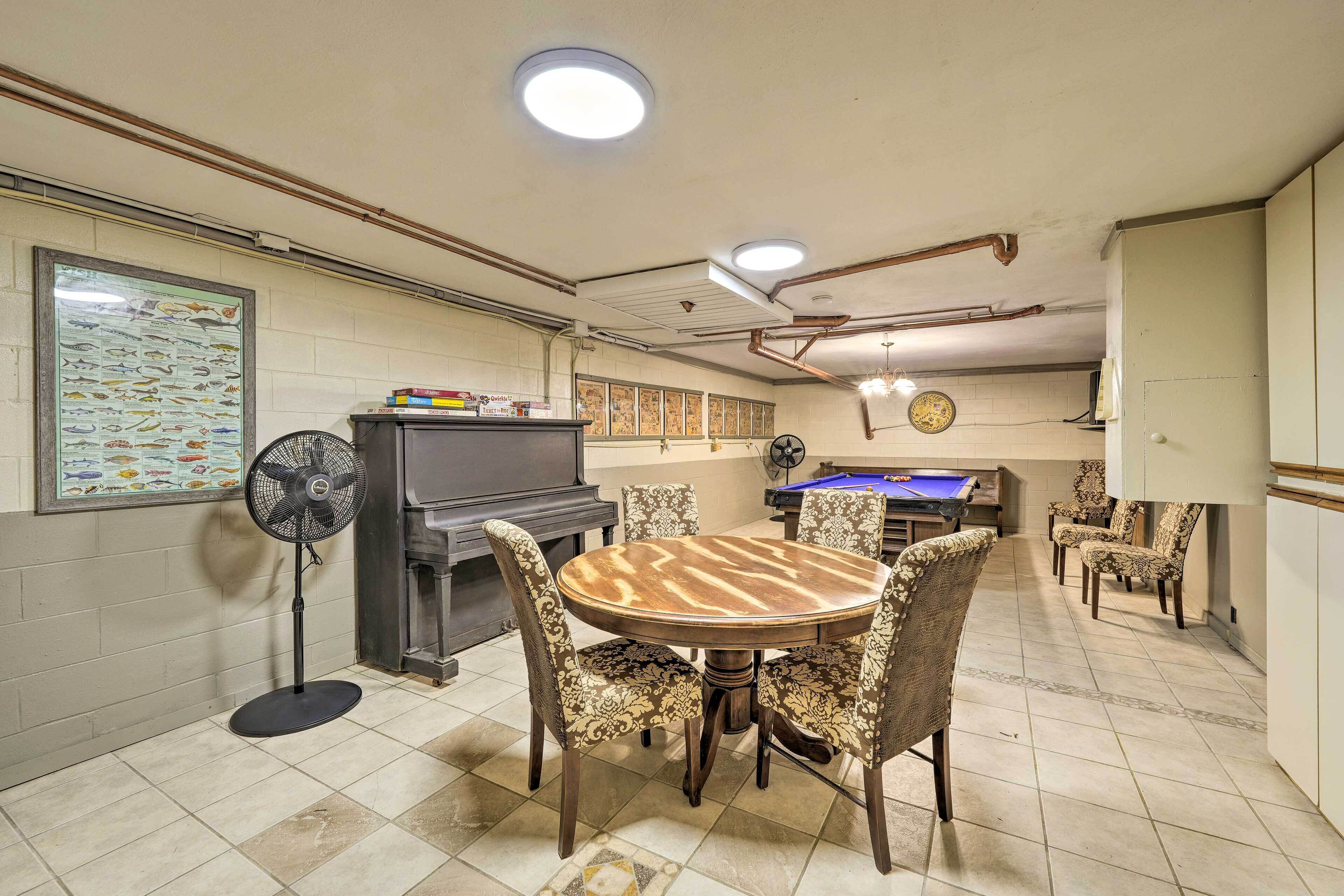 Une pièce avec une table ronde en bois, entourée de chaises à motifs, un ventilateur sur pied, un téléviseur et une table de billard.