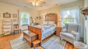 A bedroom with a wooden bed, a chair, a nightstand, a lamp, and a window with curtains. - Family Getaway w/ Pier on Currituck Sound (Currituck)