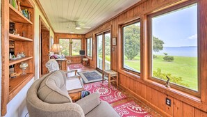 A cozy room with wooden walls, large windows, a ceiling fan, and a view of the outdoors. - Family Getaway w/ Pier on Currituck Sound (Currituck)