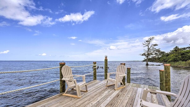 A wooden deck with three Adirondack chairs facing a calm body of water, ropes, and a tree on the right. - Family Getaway w/ Pier on Currituck Sound (Currituck)