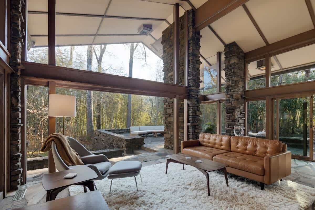 A spacious living area with a stone fireplace, leather sofa, and large windows overlooking a natural landscape.