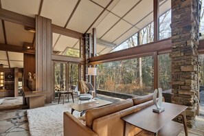 A spacious living area with a large window, a stone accent wall, and a modern seating arrangement. - Luxury Fay Jones Home - Hot Tub - Movie Theater (Memphis)
