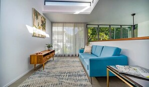 A modern living room with a blue sofa, a wooden side table, and a patterned rug.
