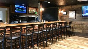 Un espace bar avec un comptoir en bois, des tabourets de bar, un téléviseur fixé au mur et une étagère remplie de bouteilles.