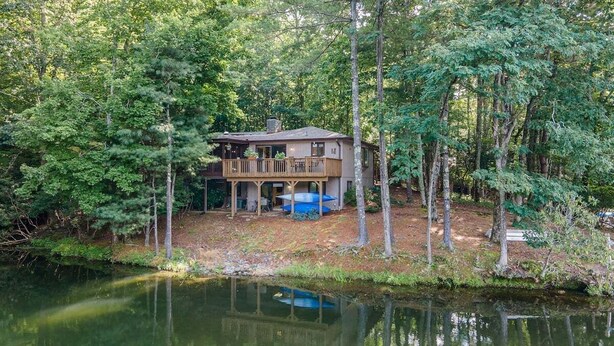 Une cabane dotée d’une terrasse, entourée d’arbres et bordée par un plan d’eau.