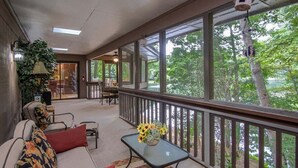 Une véranda abritée avec un canapé, des fauteuils, une table ornée d’un vase et une vue sur les arbres.