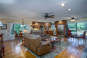 A spacious living area with a sofa, dining table, and chairs, a kitchen with wooden cabinets, and a balcony with outdoor seating.