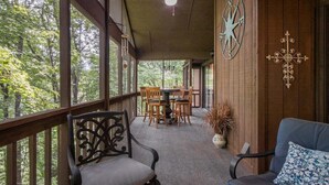 A covered porch with a dining table and chairs, a ceiling fan, and a compass wall decoration. - Peace of Heaven in Connestee Falls (Brevard)
