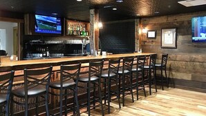 A bar area with a long counter, multiple bar stools, a television mounted on the wall, and a shelf with bottles. - Peace of Heaven in Connestee Falls (Brevard)