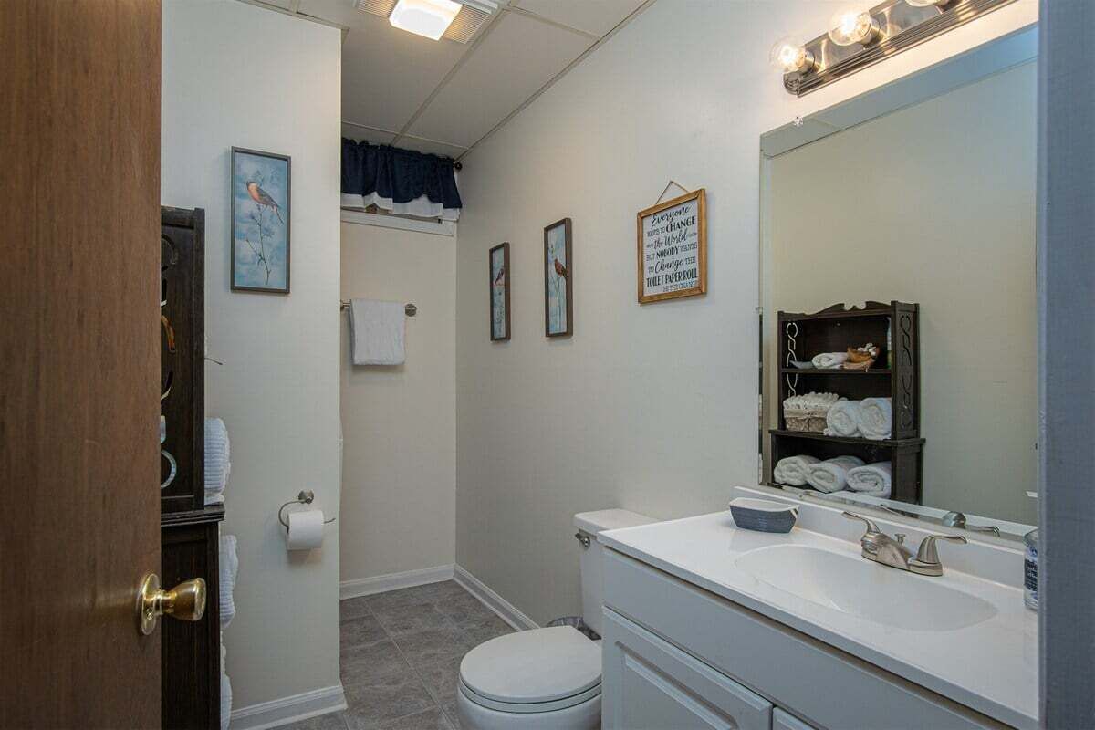 Une salle de bain avec des toilettes, un lavabo et un miroir. On y trouve des serviettes et une étagère avec des articles de toilette.