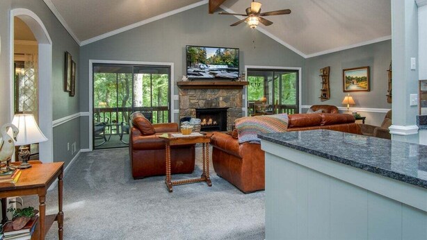 A spacious living area with a stone fireplace, leather sofas, a dining table, and a kitchen island. - Peace of Heaven in Connestee Falls (Brevard)