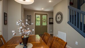 Comedor con mesa de madera, sillas, un jarrón con plantas de algodón, un reloj de pared y una escalera.
