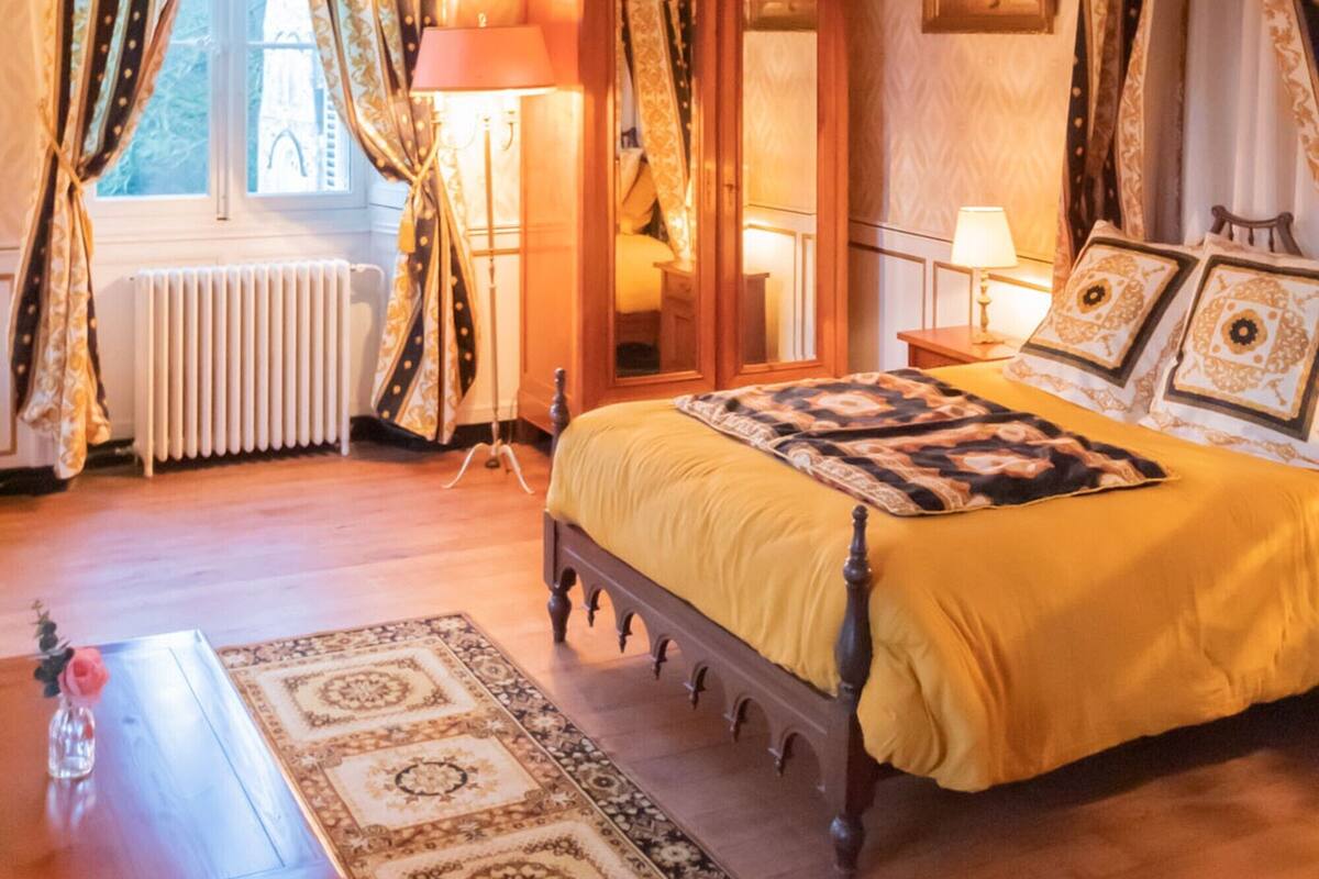 Quarto com cama de madeira, espelho, radiador e janela com cortinas.