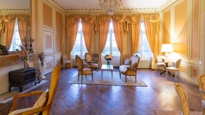 A spacious room with wooden flooring, a chandelier, and a large window with curtains. - Chateau du Hallay (Montaigu-Vendée)