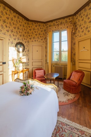 A bedroom with a large bed, a small table, two chairs, a mirror, and a window with curtains. - Chateau du Hallay (Montaigu-Vendée)