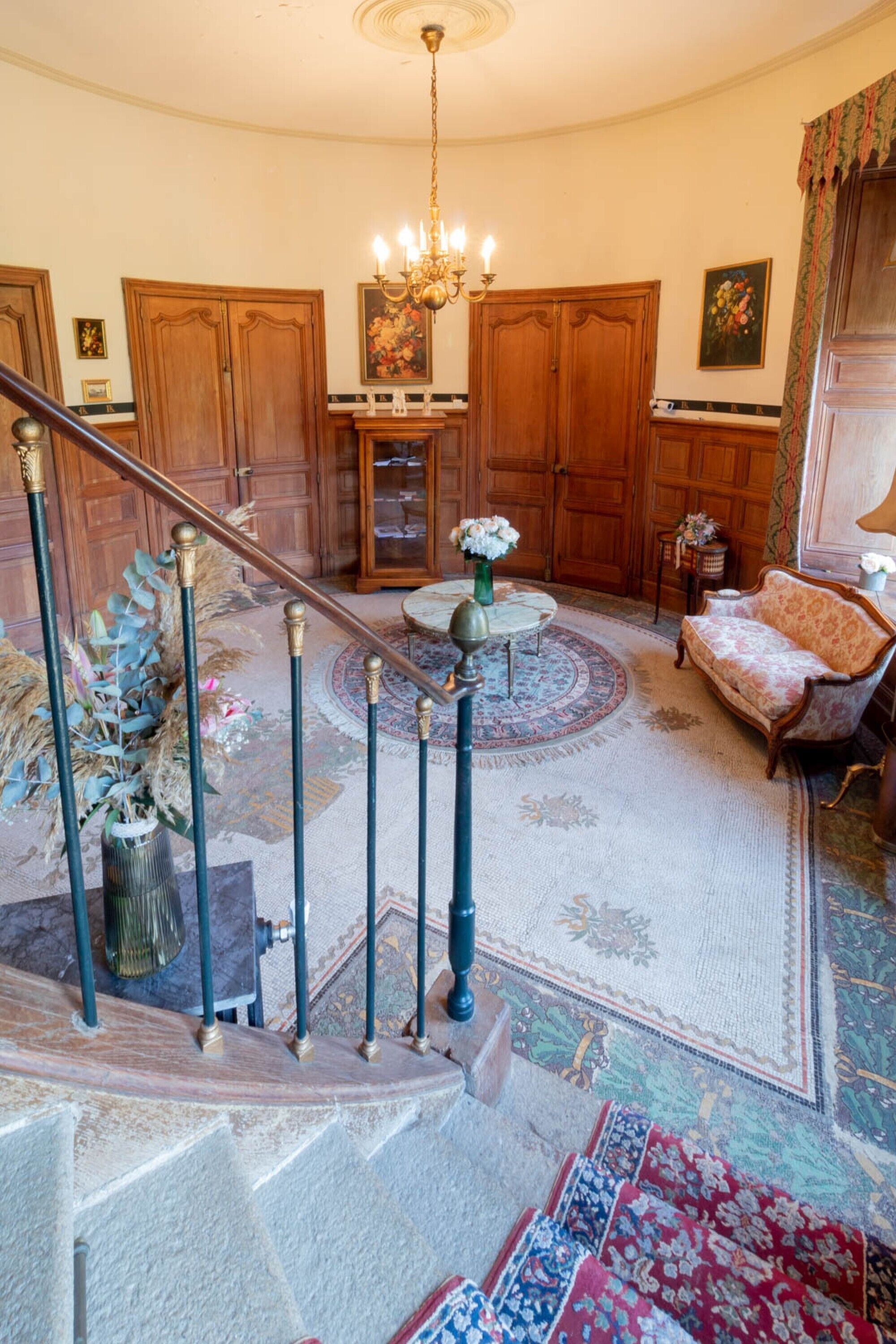 A grand staircase with a chandelier, wooden doors, and a patterned rug.