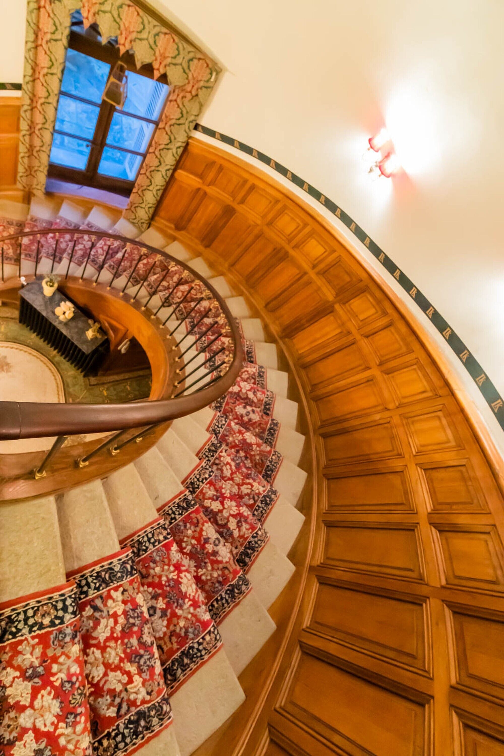 Una imponente escalera de caracol con barandillas de madera decoradas y un tapete con motivos florales.
