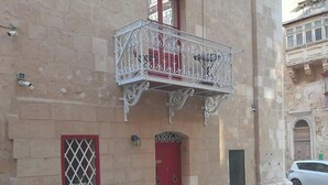 A building with a red door, a balcony with ornate metal railings, and a security camera on the wall. - 2 Bed House Sleeps 3 - Wifi, Aircon, Balcony (Valletta)