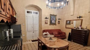 A dining area with a wooden table and chairs, a red sofa, a chandelier, and a large mirror. - 2 Bed House Sleeps 3 - Wifi, Aircon, Balcony (Valletta)