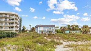 Una propiedad frente a la playa con un edificio grande, una construcción más pequeña y una zona arenosa con vegetación.