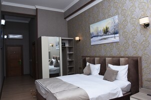 Habitación de hotel con una cama grande, un armario, un espejo y un cuadro en la pared.
