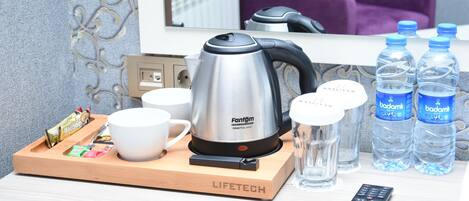 A hotel room with a kettle, cups, water bottles, a tray with snacks, and a remote control.