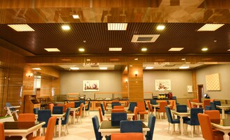 Un amplio vestíbulo de hotel con suelo a cuadros, varias mesas y sillas para comer, y una zona de cocina central.