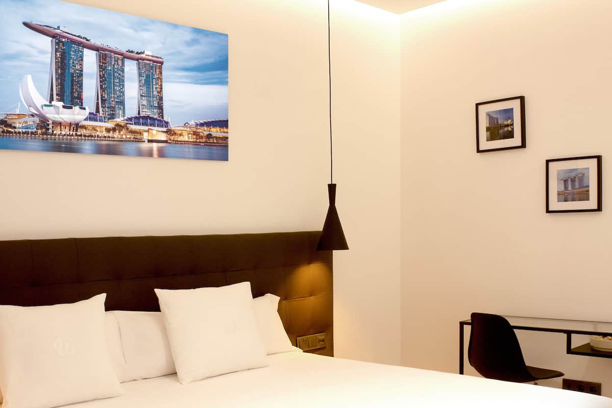 A hotel room with a bed, a desk, and a chair. There are two framed pictures on the wall.