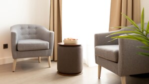 Un salón moderno con dos sillones grises, una mesita redonda con un frutero y una planta en maceta.