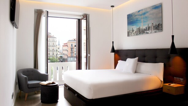 Una habitación de hotel con una cama grande, una silla, una mesita y un cuadro en la pared.