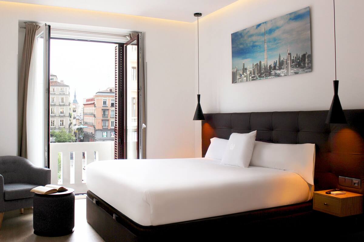 A hotel room with a large bed, a chair, a small table, and a painting on the wall.