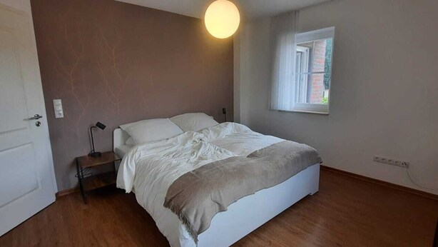 A bedroom with a bed, a bedside table, a lamp, a window, and a door. - The Eichengold Hideaway (Handrup)