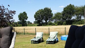 A patio area with wicker furniture, including chairs and a table, set against a backdrop of a grassy field and trees. - The Eichengold Hideaway (Handrup)