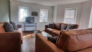 A living room with two brown leather sofas, a glass coffee table, and a TV on a stand. - The Eichengold Hideaway (Handrup)