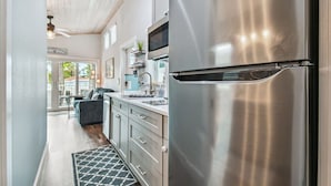 A modern kitchen with stainless steel appliances, a gray countertop, and a view to a dining area. - Surf Shack Tiny Home on Pinellas Trail w/ Heated Pool! Walk or Bike to Downtown Dunedin! (Dunedin)