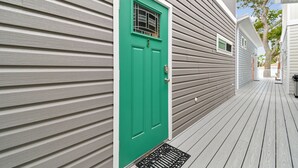 Une terrasse en bois avec une porte verte et une fenêtre ornée d’une grille métallique.