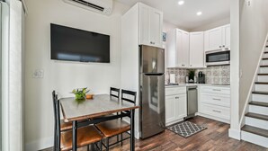 Une cuisine moderne avec des meubles blancs, un réfrigérateur en acier inoxydable, un four à micro-ondes et un coin repas comprenant une table et des chaises en bois.