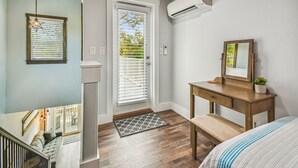 Une chambre à coucher avec un bureau en bois, un lit, une fenêtre avec des stores, une porte et un appareil de climatisation.