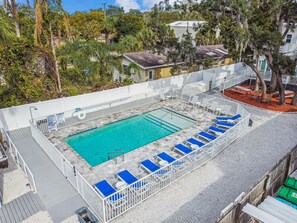 Une piscine rectangulaire avec une terrasse blanche et des chaises longues bleues.