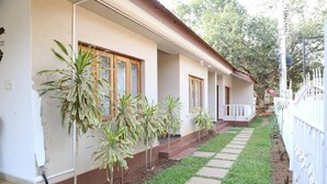 A single-story house with a covered porch, a small garden with potted plants, and a white fence.