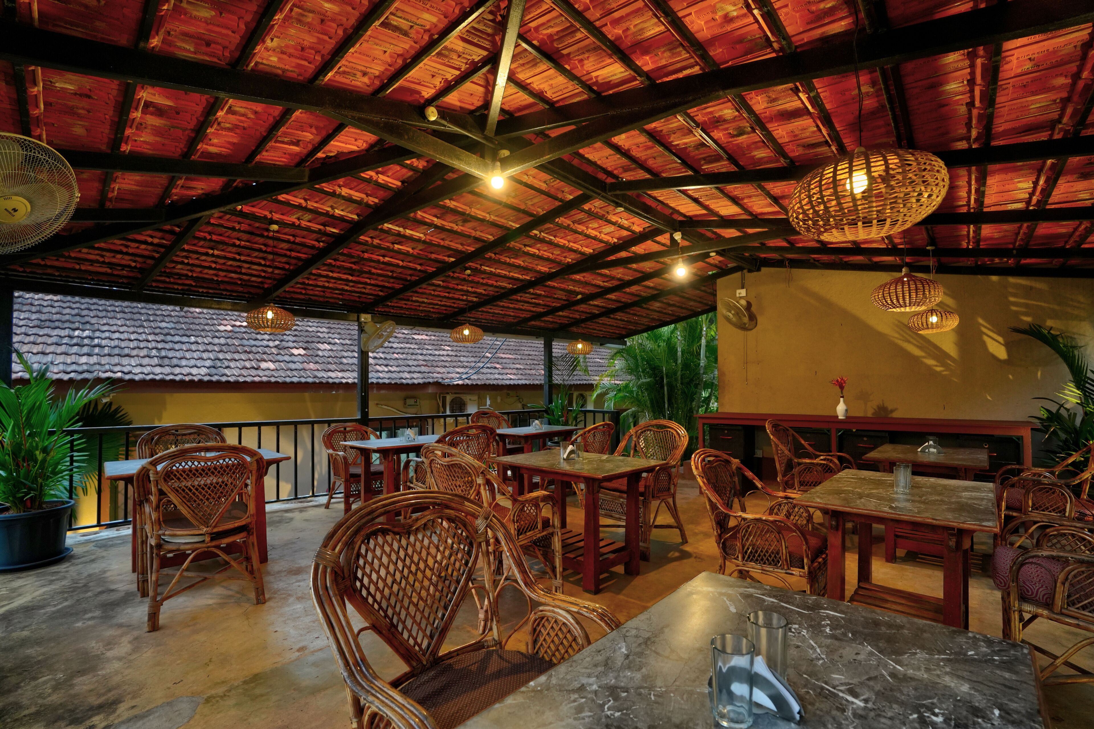 An outdoor dining area with wicker furniture, a tiled floor, and a red-roofed ceiling.