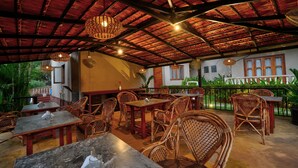 An outdoor dining area with wicker furniture and a red roof. Tables and chairs are arranged for dining.