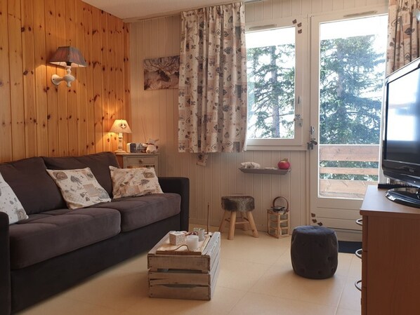 A cozy living room with a brown sofa, a wooden coffee table, a television, and a window with curtains.