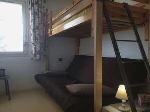 A bunk bed room with a ladder, a sofa, a lamp, and a window with curtains.