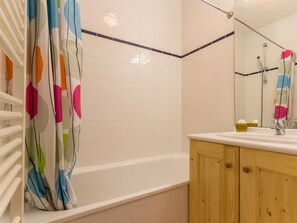 A bathroom with a bathtub, wooden cabinets, a mirror, and a shower curtain.