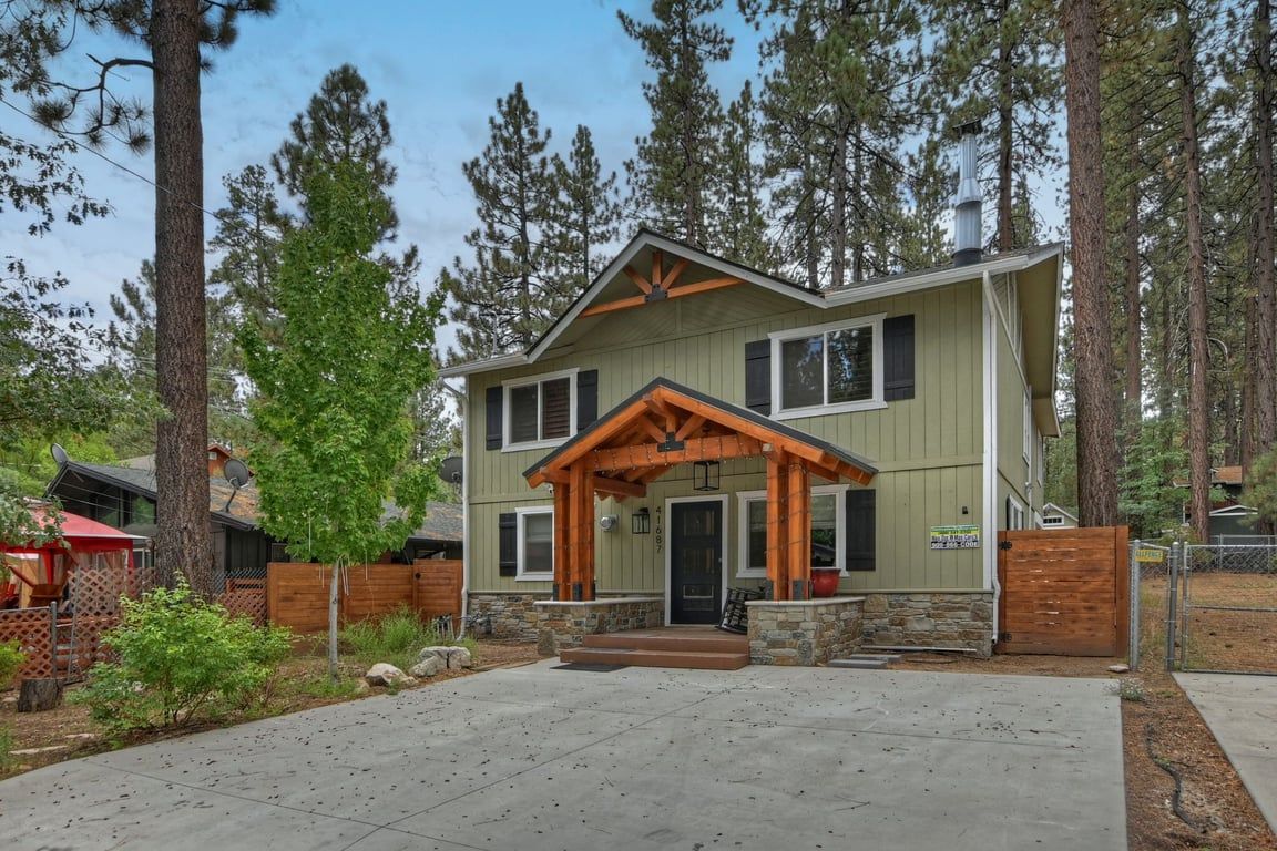 A two-story house with a porch, stone foundation, and a wooden fence.